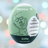 Image of a green and black egg-shaped product labeled "Satisfyer 'Riffle' Penis Stroker Egg." The packaging features a line drawing of a face in black and an illustration of the internal cyber-skin texture. The background is softly blurred with colorful bokeh lights, highlighting its sophisticated design.